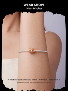 Detailed view of silver mesh bracelet with orange pumpkin charm on model wrist