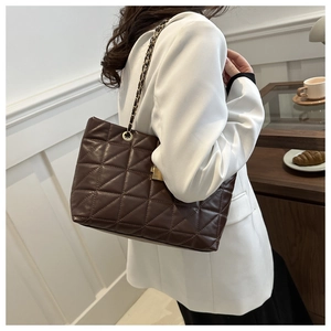 Close-up of a large dark brown quilted chain tote bag worn by a model in a cafe setting