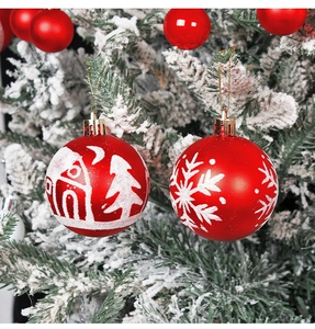 Close-up of red Christmas baubles with white glitter snowflakes on snowy pine branches