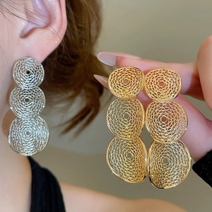 Macro detail of geometric hollow round pendant earrings in silver and gold finishes