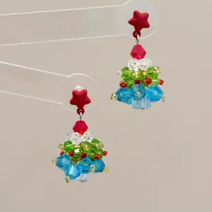 Close-up of handmade beaded Christmas tree earrings with red bow and colorful crystals