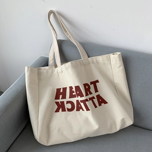 Close-up of beige canvas tote bag featuring a red Heart Attack letter print design