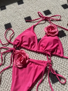 Flat lay of pink bikini featuring 3D silk flower accents and side-tie bottoms