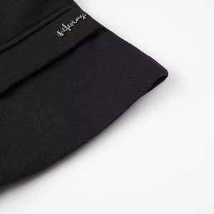 Close-up of black woolen jacket texture featuring a small silver metal brand tag