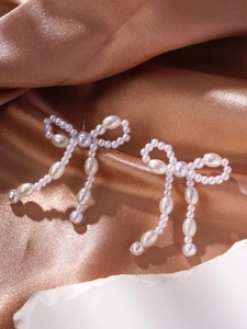 Detailed view of elegant bow-shaped pearl tassel earrings on a warm silk background