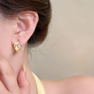 Close-up of a sweet cream enamel bow earring worn on an ear for a dainty and elegant look.