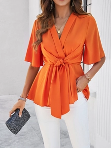 Détail du chemisier orange à col en V avec taille nouée et manches cloches élégantes