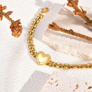 Elegant gold stainless steel heart charm bracelet on white marble base with natural branches