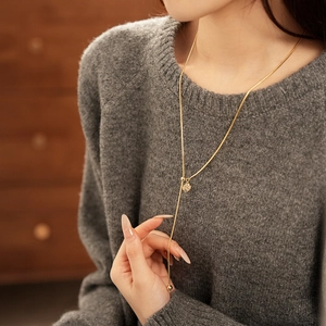 Close-up of a gold-plated Y-shaped tassel necklace with zircon on a gray knit sweater