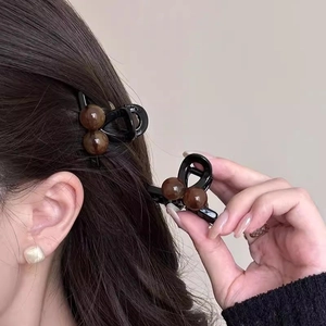 Detail of a black hair clip with brown bead accents held by a hand and worn by a model