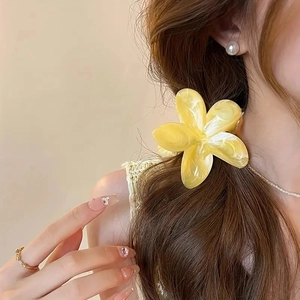 Detail of yellow plumeria hair claw with pearlescent finish worn on hair for vacation