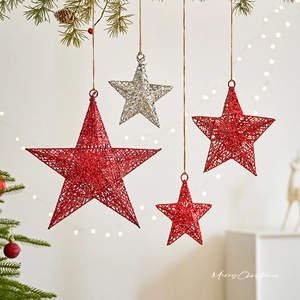 Christmas star ornaments in red and silver hanging on pine branches with warm lights