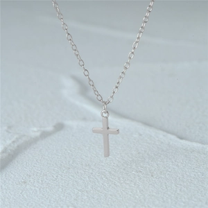 Macro shot of minimalist silver cross pendant on a fine chain with matte background
