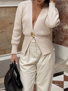 Dettaglio del cardigan in maglia beige con scollo a V profondo e bottone dorato unico