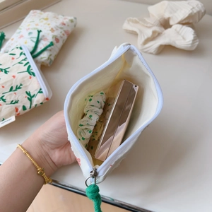 Detail view of cotton floral mini coin pouch with green rope zipper and beige fabric texture
