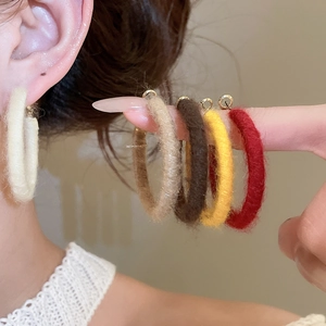 Macro shot of colorful textured yarn-wrapped hoop earrings on beige background