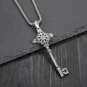 Macro shot of large silver key pendant with intricate patterns on a dark stone surface