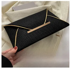 Détail d'une pochette enveloppe noire à motif crocodile avec bordures dorées