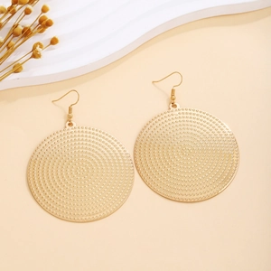 Detailed view of large gold round earrings with textured polka dot surface and ear hooks