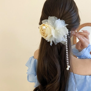 Detailed close-up of lace rose hair clip with long pearl tassels on wavy brown hair