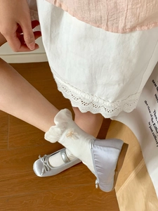 Close-up of silver Mary Jane shoes with bow detail and white lace cotton socks for girls
