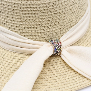 Macro detail of straw hat featuring cream chiffon ribbon and colorful rhinestone ring