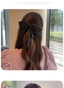 Detail of a large black satin bow hair clip with long ribbons on a model's hairstyle