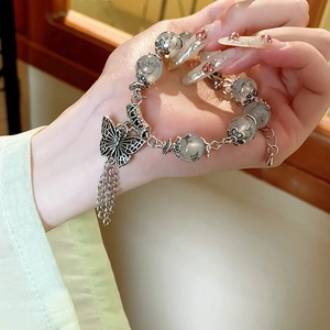 Détail du pendentif papillon argenté et des glands sur le bracelet perles à encre