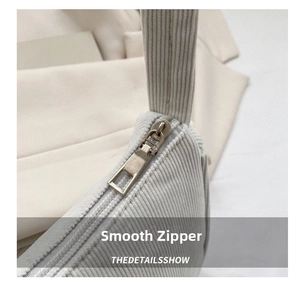 Macro detail of smooth metal zipper and ribbed corduroy texture on the beige bag