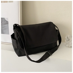 Detail of black nylon messenger bag featuring adjustable wide strap and minimal workwear style