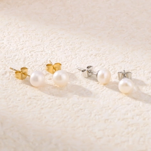 Close-up of elegant gold and silver pearl stud earrings on a beige textured surface