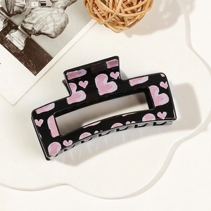 Detail view of a black rectangle hair claw clip with pink heart prints on a retro background