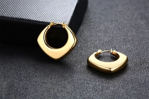 Macro shot of polished gold square hoop earrings on a textured dark background