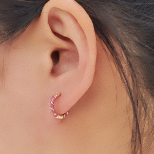Pink enamel twisted hoop earrings in gold plating shown on a model for a chic look