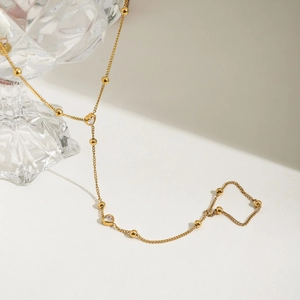 Detail of 18K gold-plated hand chain with heart zircon and beads near crystal glass