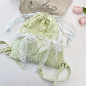 Close-up of light green drawstring backpack with white lace bows and floral texture