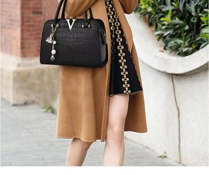 Close-up of black crocodile pattern leather handbag with gold V logo and pearl pendant detail