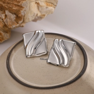 Macro shot of silver square earrings with wave texture on minimalist ceramic surface
