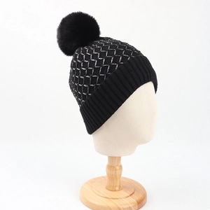 Detailed view of black knitted beanie with silver tinsel grid and large faux fur pom-pom