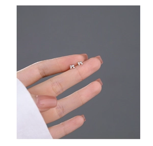 Macro shot of a tiny silver bow earring on a fingertip showing its miniature size