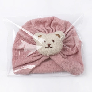 Detailed view of a soft pink baby knitted turban hat with cute plush bear in packaging