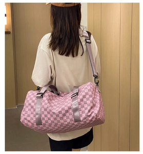 Pink checkerboard travel bag with grey strap shown on model in a modern hallway