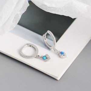 Macro shot of silver hoop earrings featuring blue opal charms and sparkling zircon accents