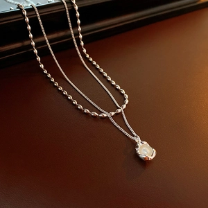 Detail of silver double-layer necklace with pearl pendant on brown leather background