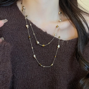 Detail of 18k gold plated necklace with tiger eye stone and pearls on brown knitwear