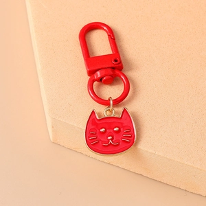 Close-up of a red cat charm keychain with gold metal edges on a beige display surface