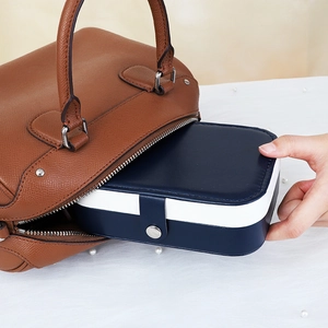 Portable jewelry box in blue and white being placed in a brown leather handbag