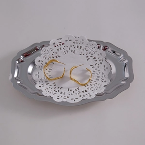 Macro shot of 18k gold-plated wavy hoop earrings on a vintage metal tray with lace detail