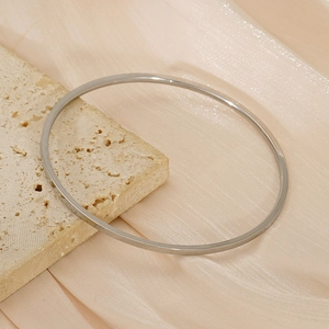 Minimalist silver titanium steel bangle displayed on a beige stone with silk background
