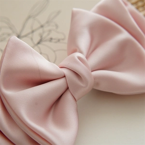 Macro shot of pink satin bow hair clip showing smooth silk texture and hand-knotted detail